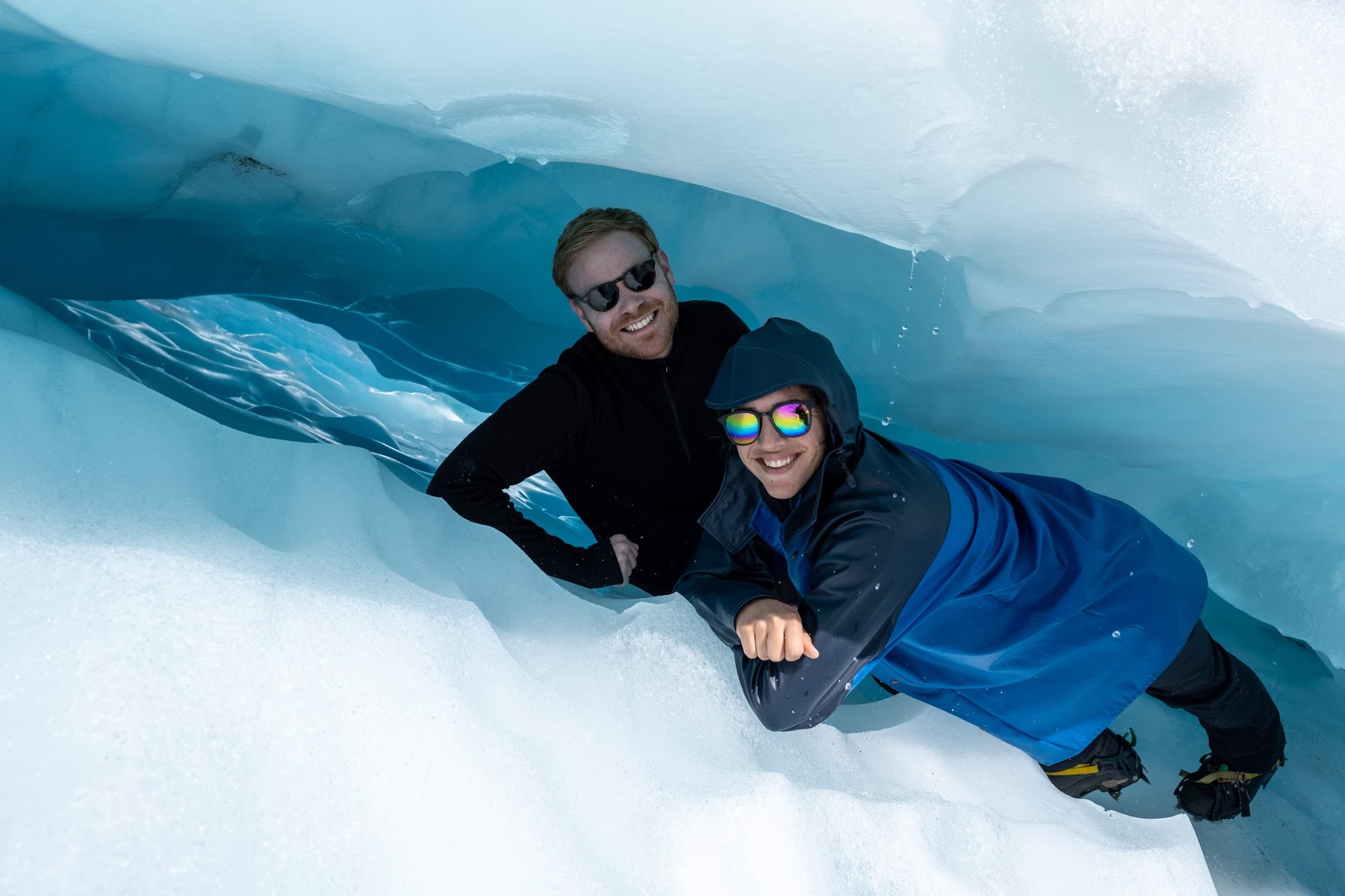 Ariana and Erik lying in a crevice in a glacier, smiling up at the camera